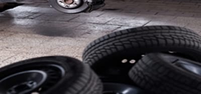 A car in the service bay with its wheel off and the brake rotor exposed, tires stacked on the shop floor
